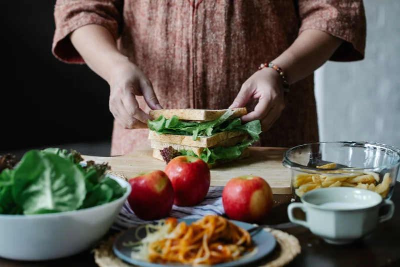 Crop faceless female in casual clothes standing near table with various food and preparing dinner