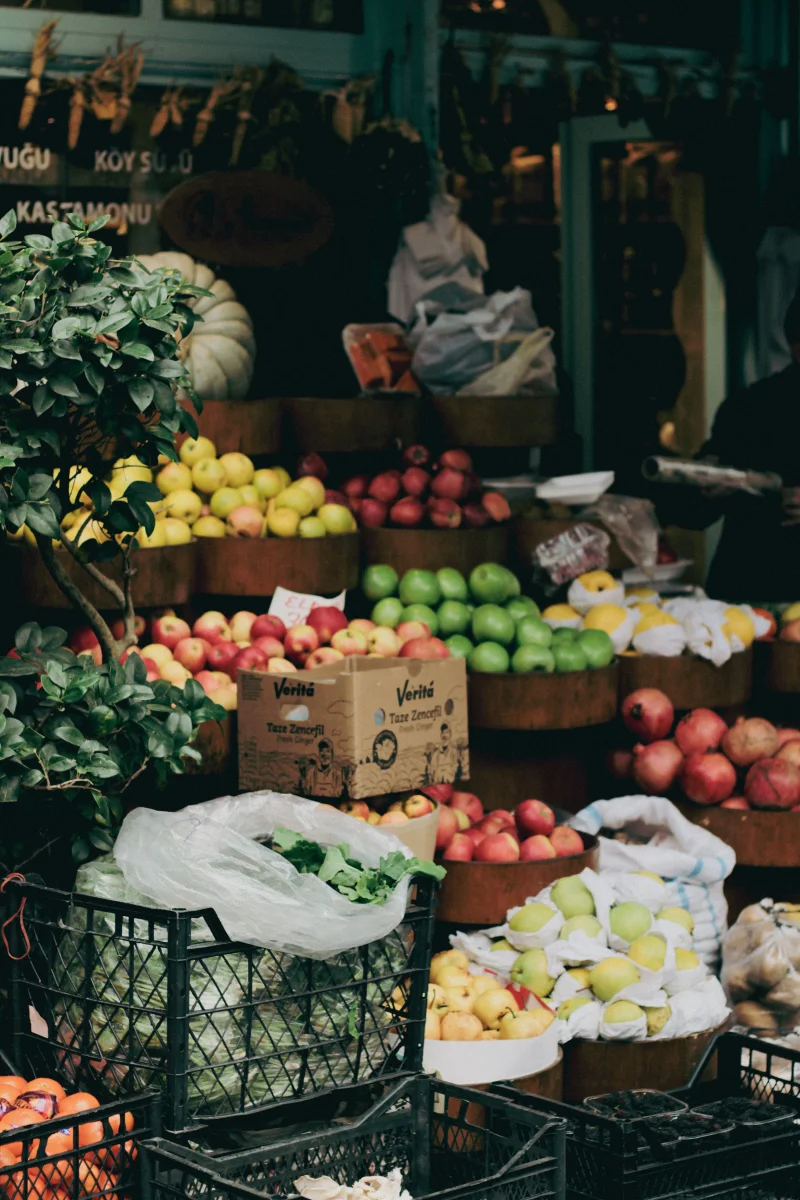 Colorful display of fresh fruits and vegetables at an outdoor market stall, showcasing apples, lemons, and greens.