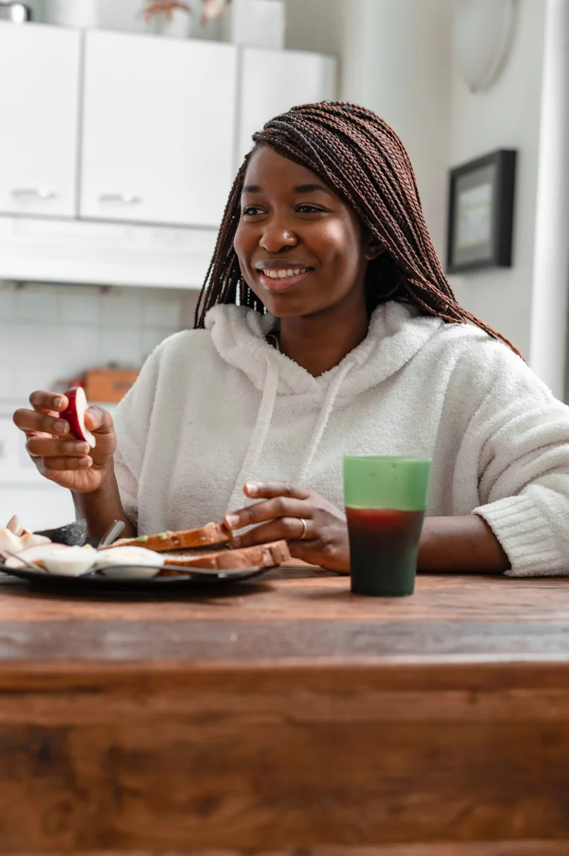 A woman in a hoodie smiles as she enjoys a healthy breakfast with apple slices indoors.