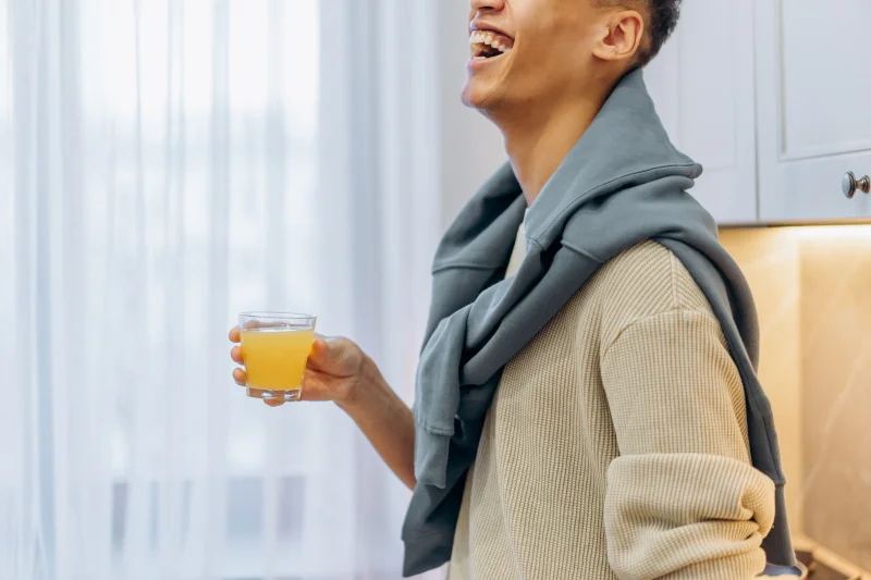Smiling man holding a glass of orange juice, standing in a cozy kitchen.