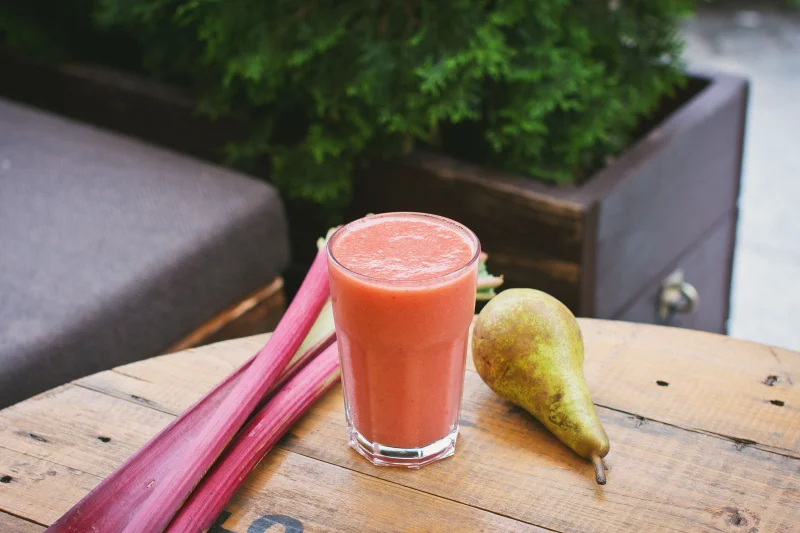 Delicious pear and rhubarb smoothie in a glass on a wooden table, perfect for summer refreshment.