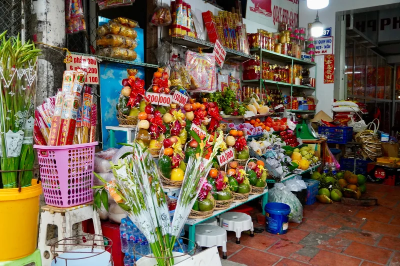 Colorful Vietnamese market stall with fruit arrangements, fresh produce, and cultural items.