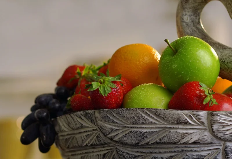 Close-up of assorted fresh fruits like apples, oranges, and strawberries in a ceramic bowl.