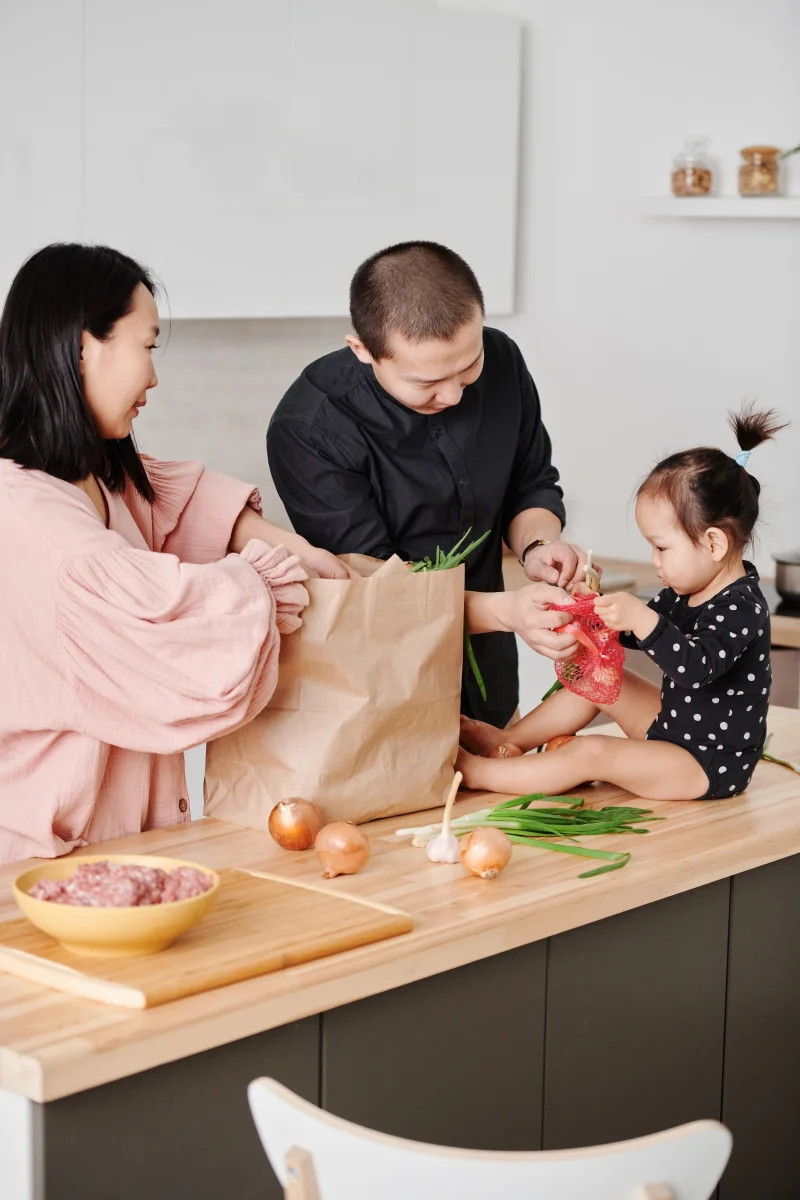 Asian family unpacking groceries on kitchen counter, sharing quality time together with vegetables and food items.