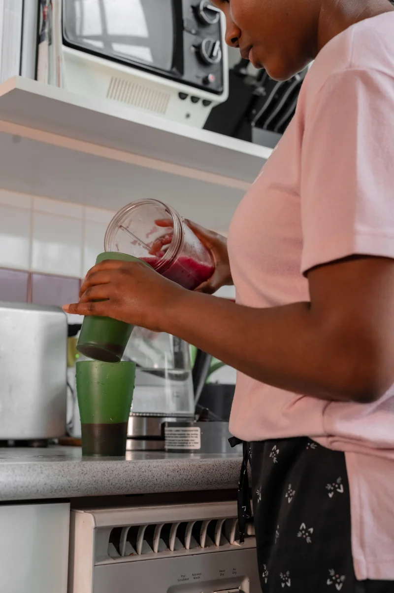 African American woman making a green smoothie in a modern kitchen setting.