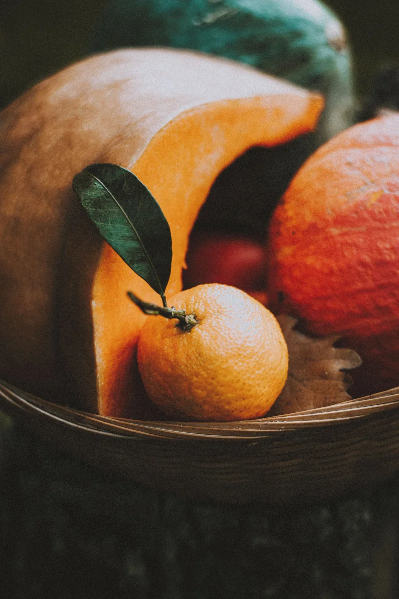 Colorful tangerine with leaf in wicker basket with cut pumpkin in soft light