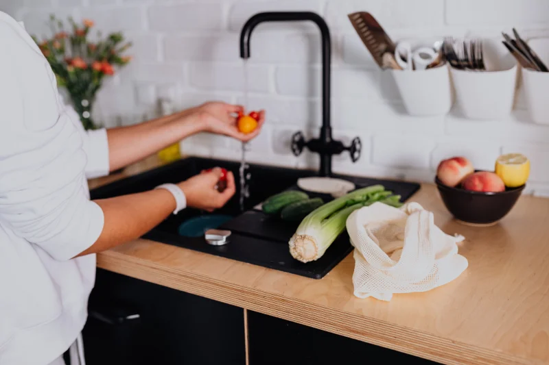 A woman washing fresh vegetables at a kitchen sink in a modern home environment.