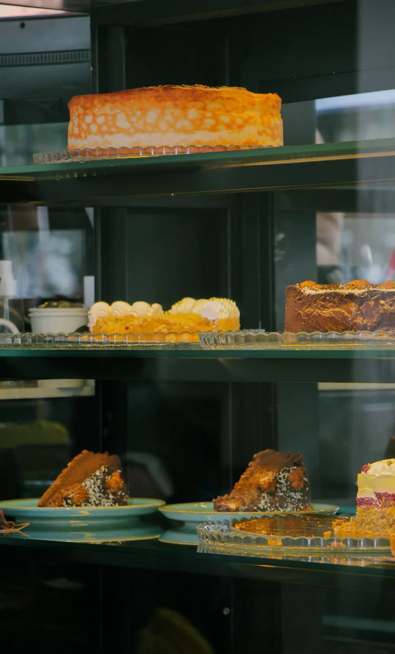 A variety of cakes on shelves in a bakery display fridge, showcasing delicious slices and whole desserts.
