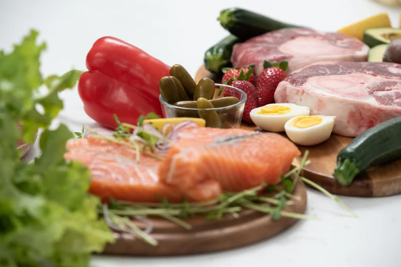 A vibrant assortment of fresh salmon, eggs, vegetables, and fruits arranged on a wooden platter.